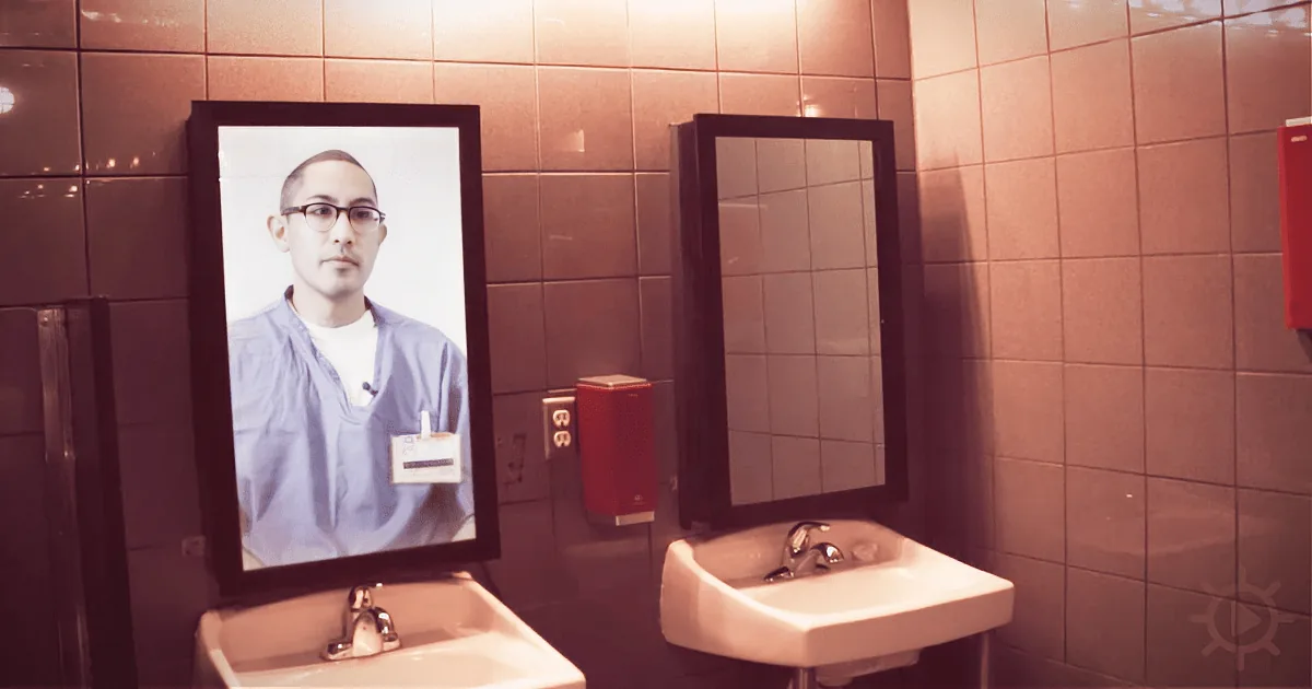 A man in scrubs is displayed on a monitor above a sink in a bathroom.