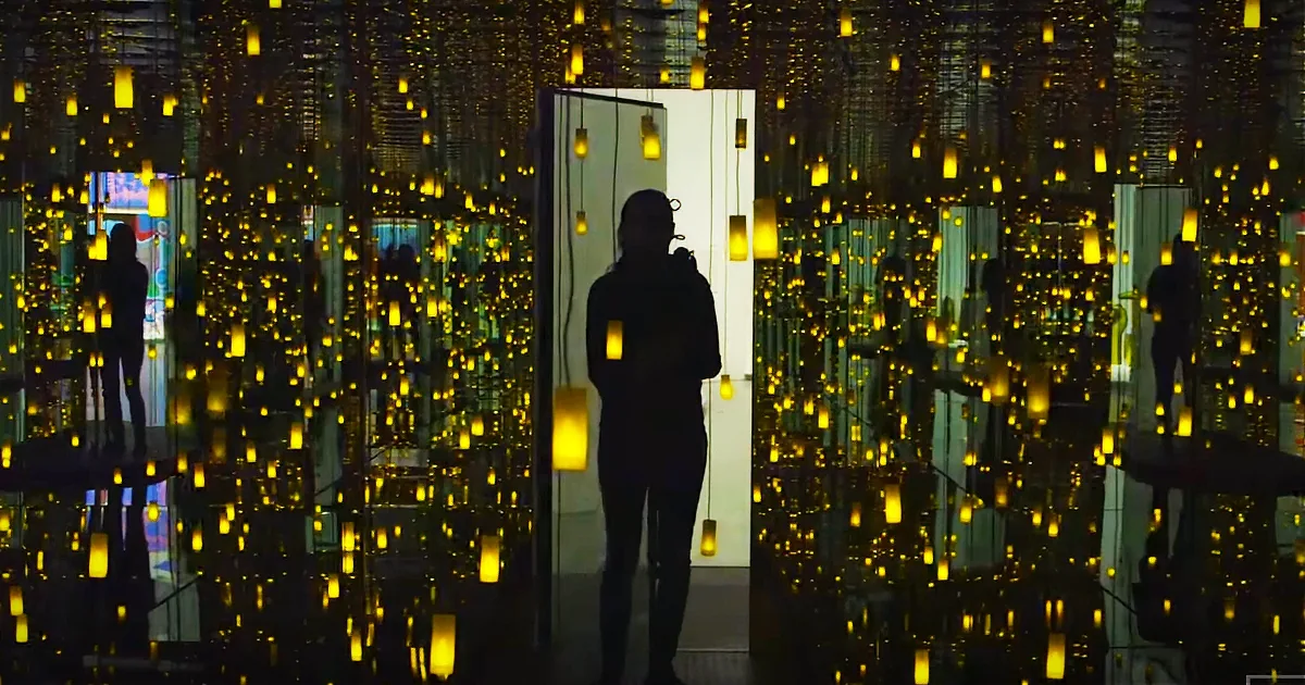 A person stands in a room filled with hanging yellow lights, creating a reflective, glowing effect.