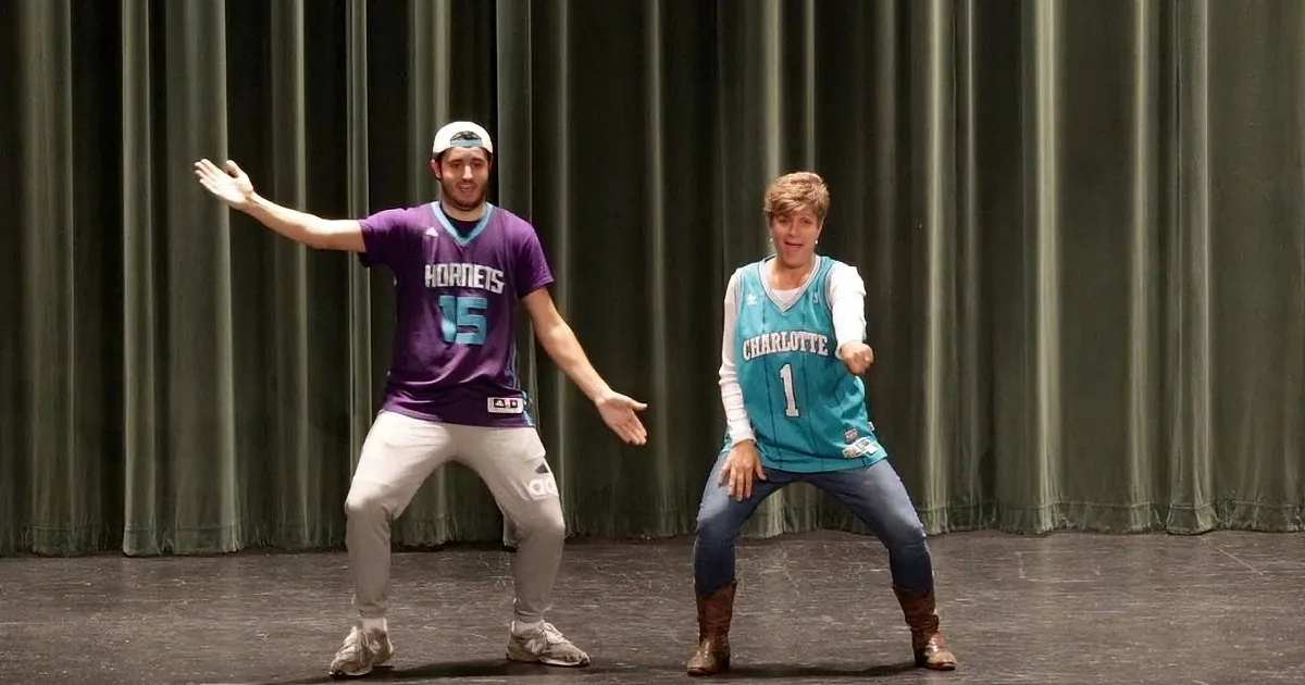 A man in a purple Hornets jersey and a woman in a teal Charlotte jersey are dancing on stage.