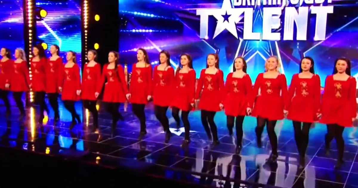 A group of women in red dresses perform on a stage with "Britain's Got Talent" backdrop.