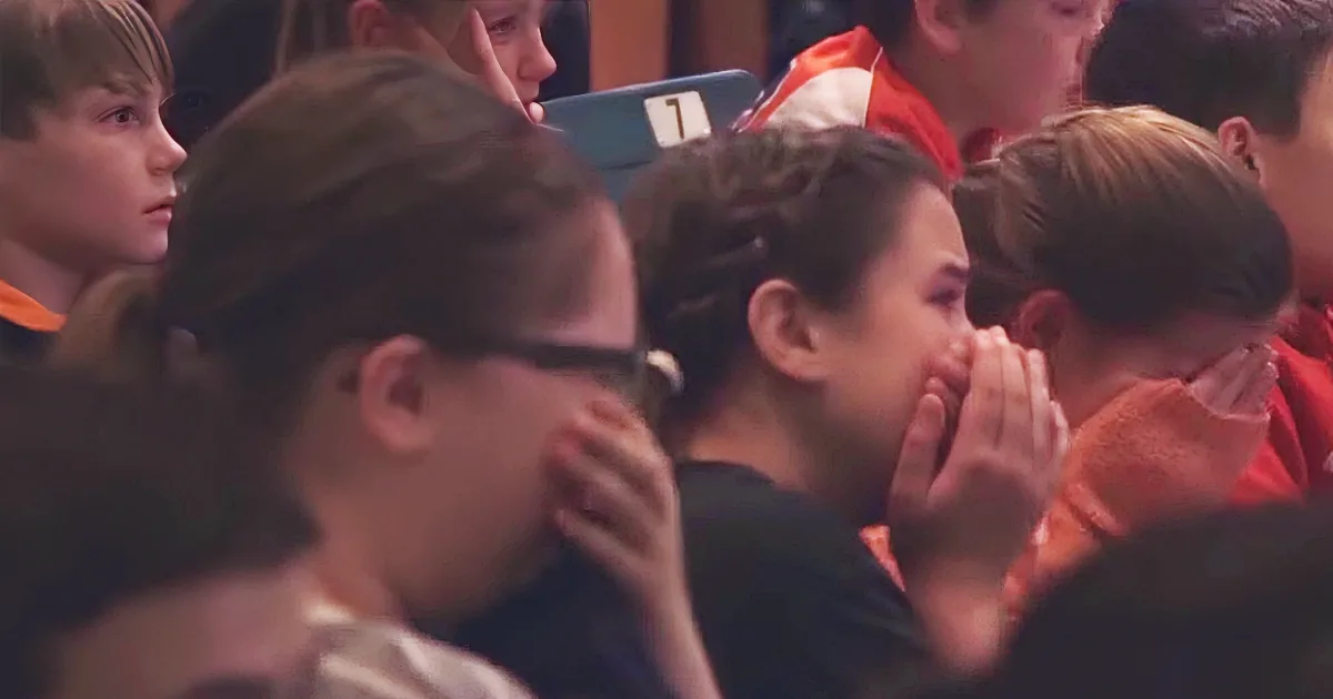 A young woman covers her mouth with her hands, appearing distressed, in a crowded audience.