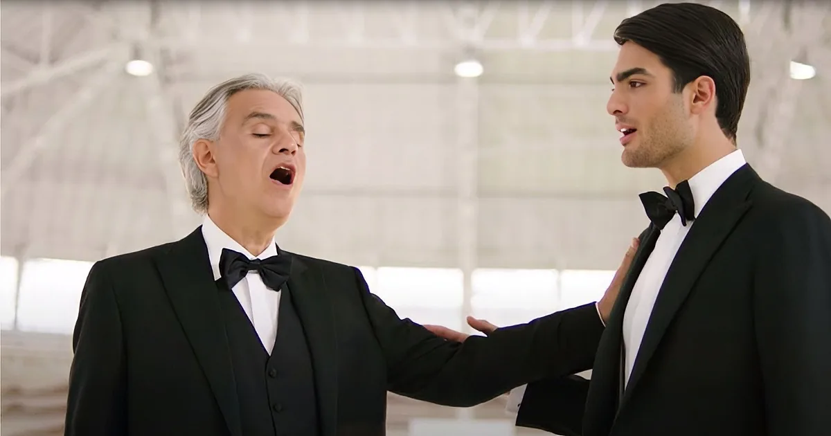 A man in a tuxedo sings passionately while another man in a tuxedo gestures beside him.