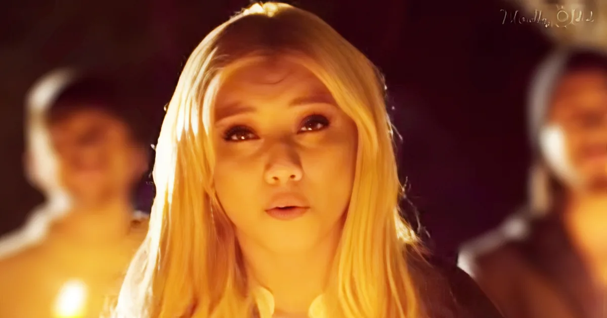 A person with long blonde hair and a white top is in focus, with two blurred figures behind them.