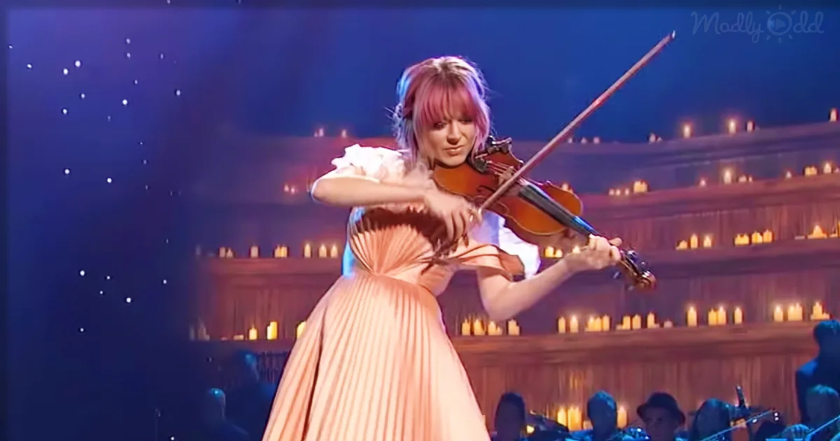 A violinist in a peach dress plays on stage with a candlelit background.