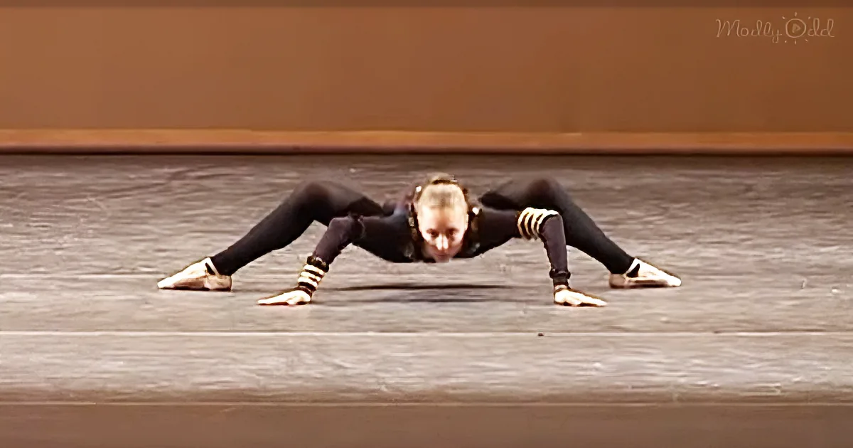 A dancer in a split position on a dance floor, wearing black attire and gold accents.