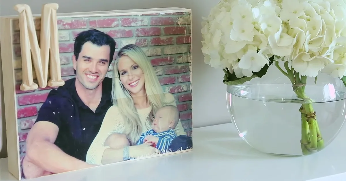 A family photo of a couple holding a baby is displayed on a white surface next to a vase of white hydrangeas.