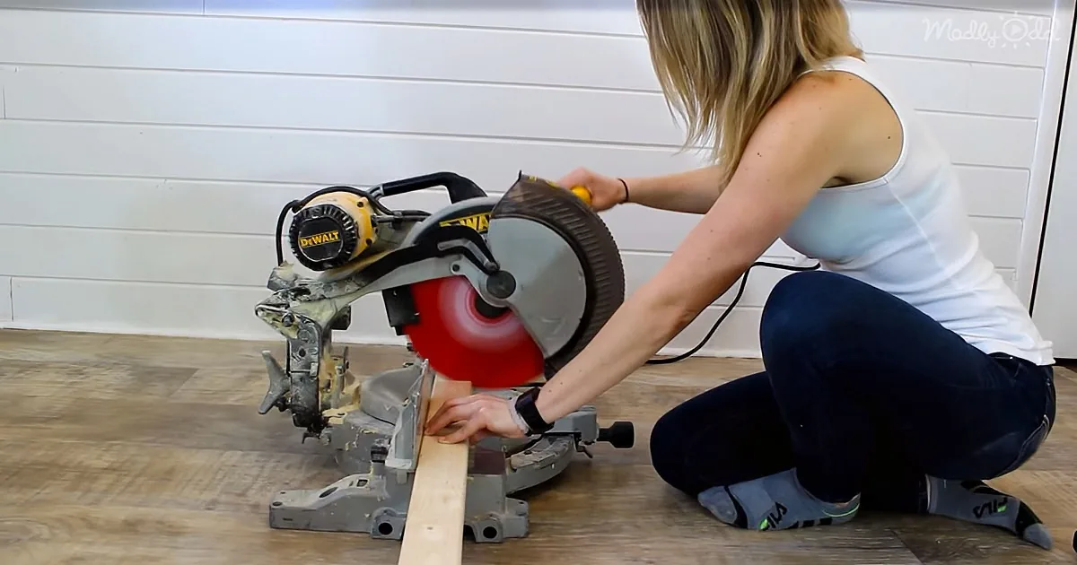 A woman kneels, using a DeWalt miter saw to cut a piece of wood on a wooden floor.