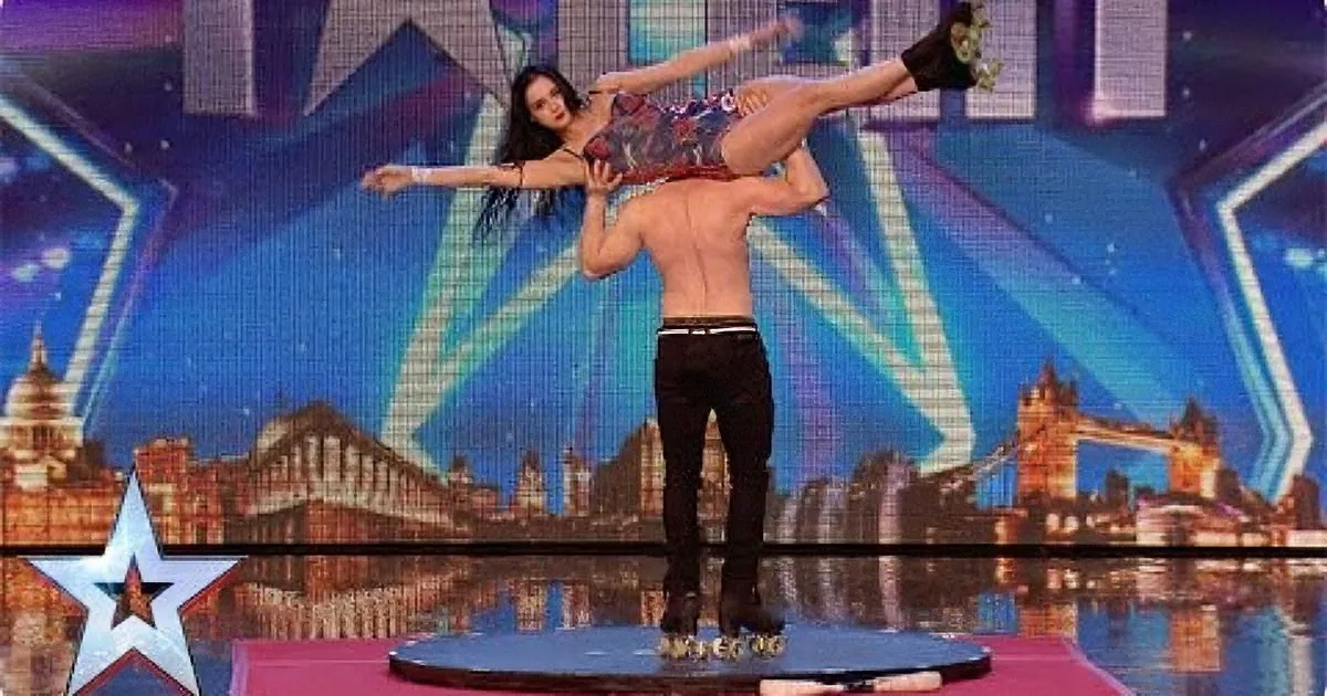 A man balances a woman on his shoulders in a dramatic acrobatic pose on a stage.