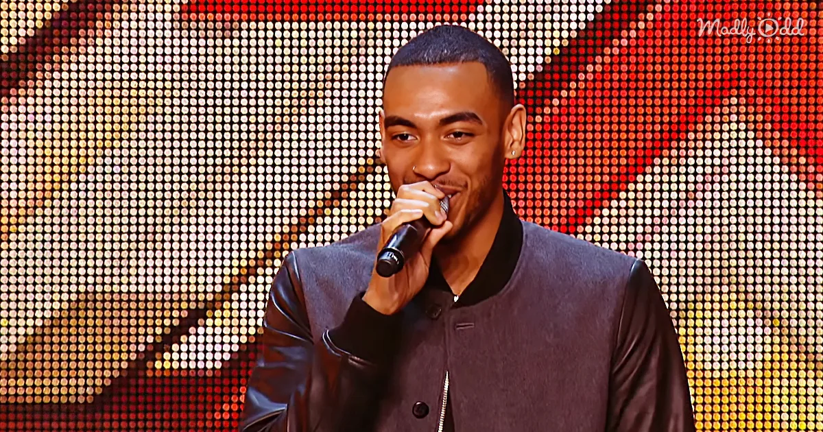 A man in a black jacket holds a microphone, smiling, against a colorful, glittery background.