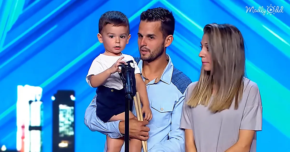 A man holds a young child on stage, both gripping a microphone, with a woman standing nearby.