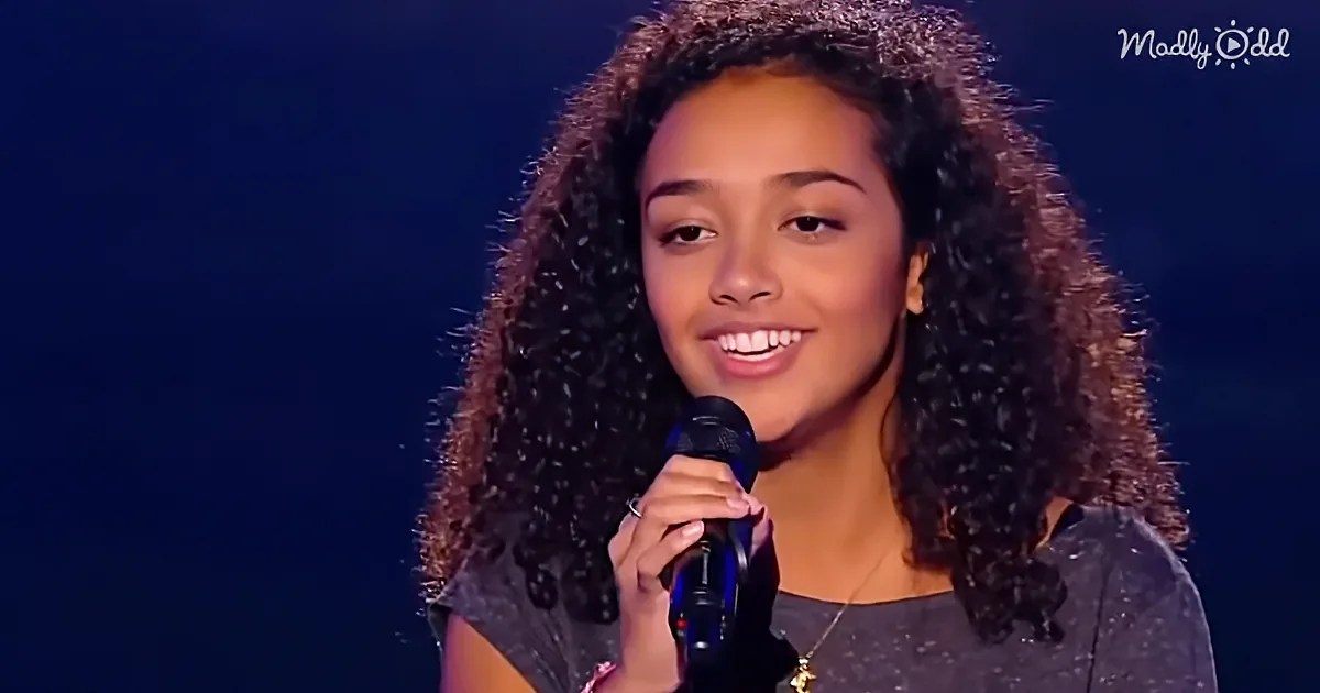 A person with curly hair smiles while holding a microphone on stage.