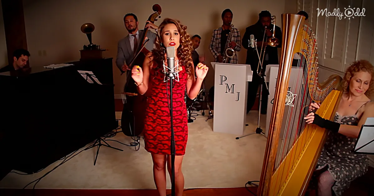 A woman in a red dress sings into a microphone, surrounded by musicians and a harpist.