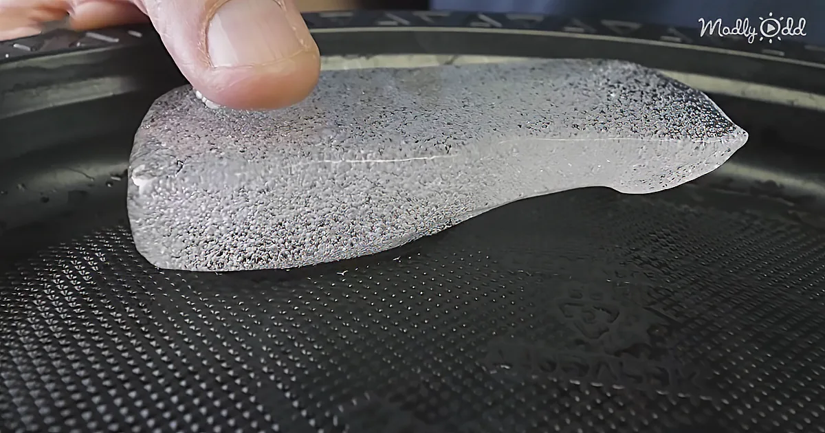 A hand holds a gray, textured object resembling a shoe insole on a black textured surface.
