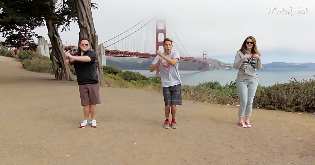 Three people stand on a path near the Golden Gate Bridge, posing with a scenic view behind them.