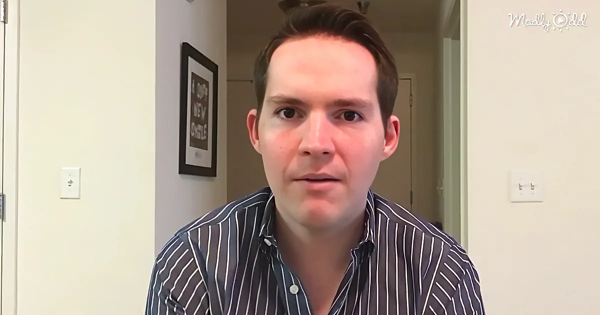 A man in a striped shirt sits indoors, looking directly at the camera with a neutral expression.