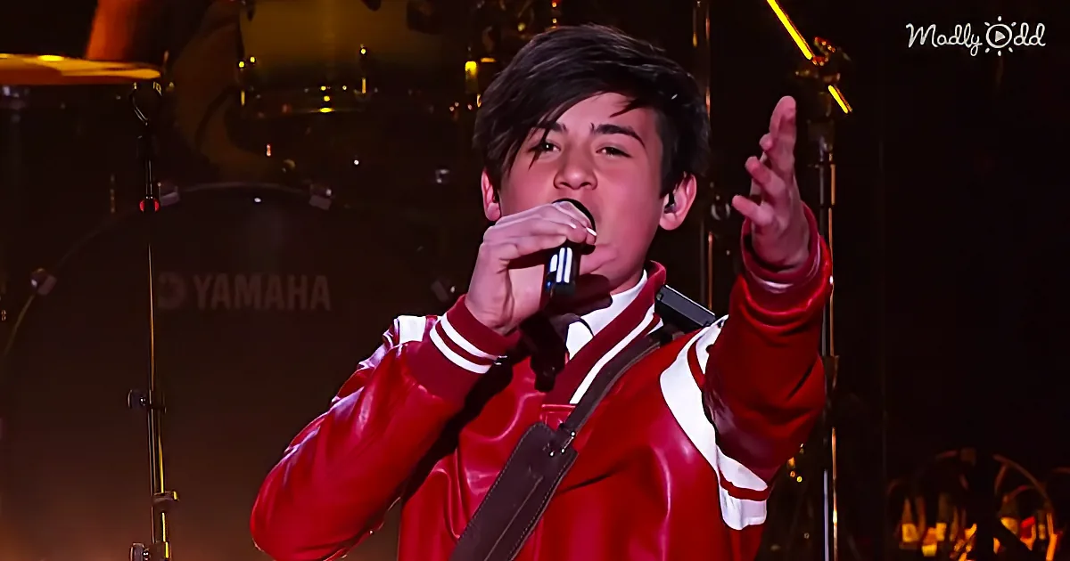 A person in a red jacket sings into a microphone, gesturing with one hand raised.