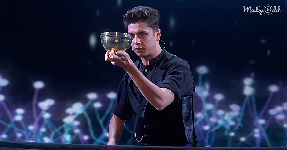 A man in a black shirt holds a glowing object, appearing surprised, against a dark, illuminated background.