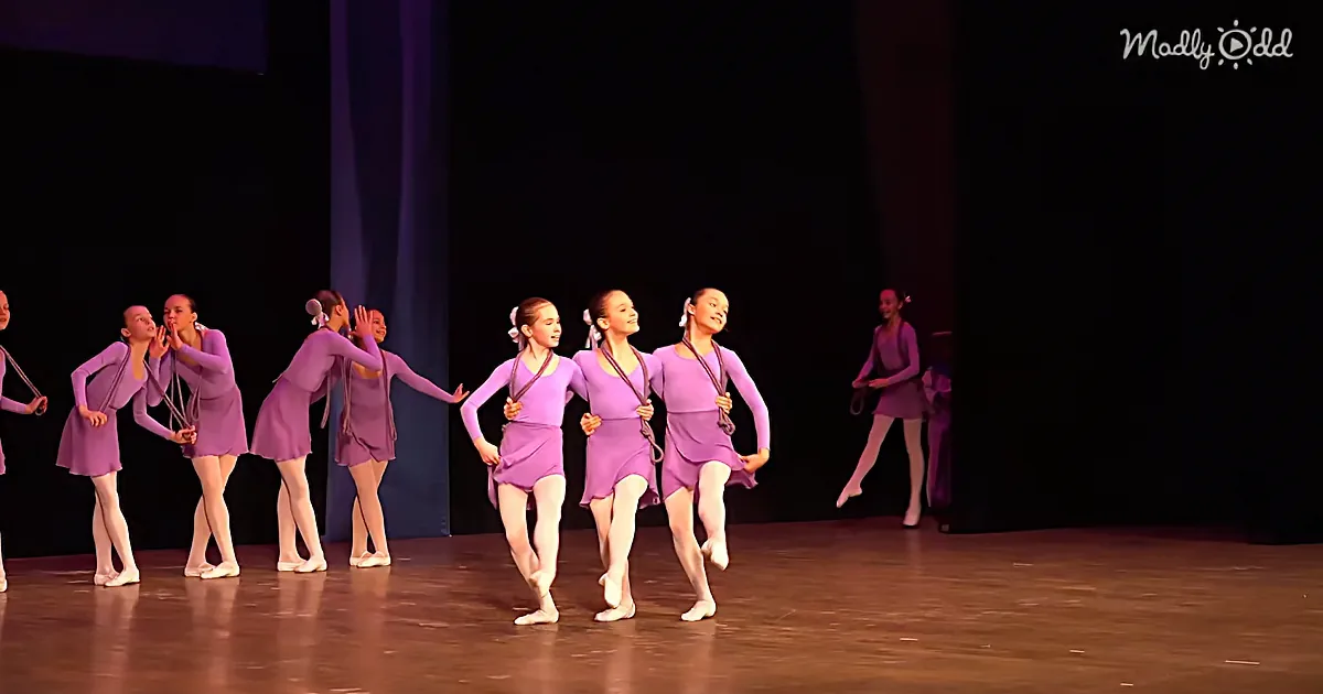 A group of dancers in purple costumes perform a synchronized routine on stage.