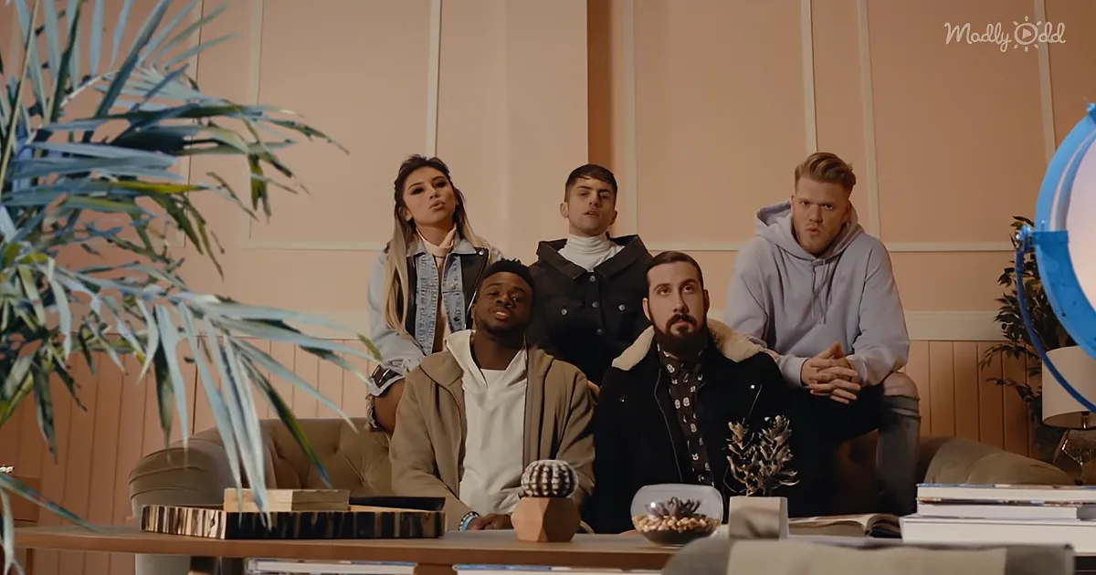 A group of five people sit on a couch in a modern room with plants and books, looking up.