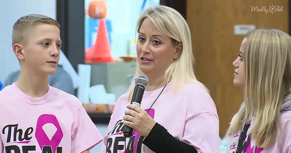 Woman in pink shirt holding microphone, standing between two children also in pink shirts.