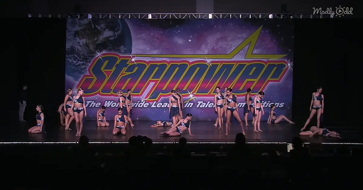 A group of performers in matching outfits are on stage in front of a "Starpower" banner.