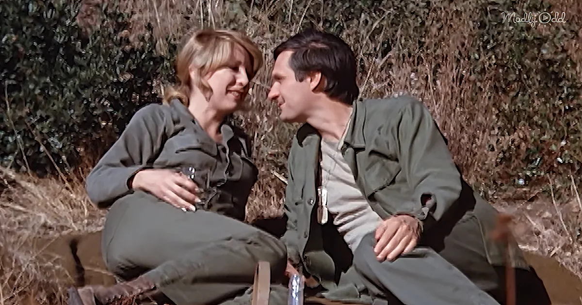 A couple in green outfits sits outdoors, smiling and holding drinks, surrounded by nature.