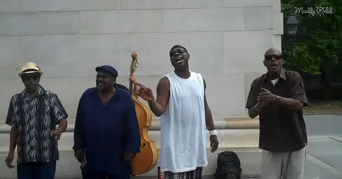 A man in a white tank top sings passionately while holding a large string instrument, surrounded by other musicians.