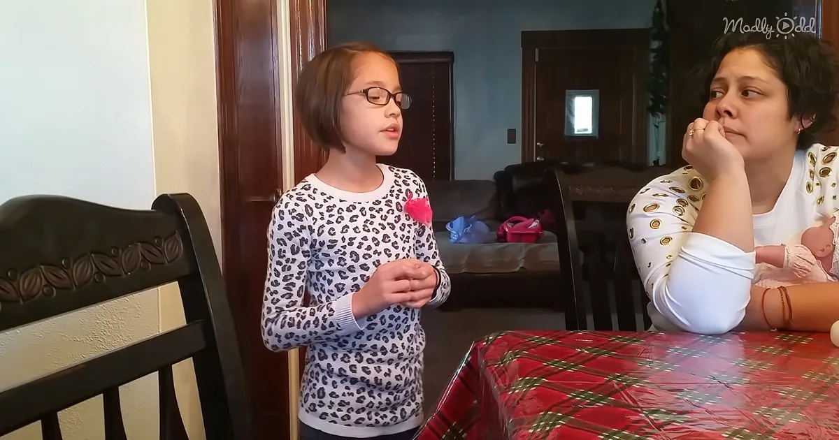 A young girl in a leopard print sweater stands at a table with a woman in a polka dot shirt, both in a home setting.