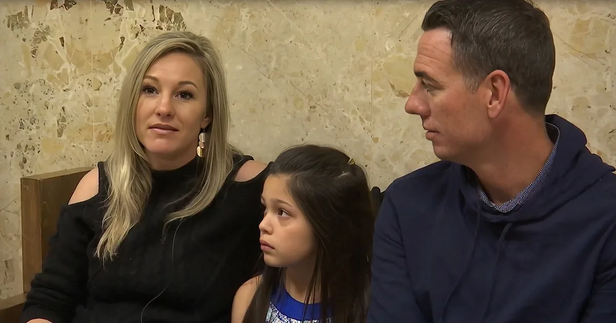 A woman in black, a girl in blue, and a man in navy blue are seated together, looking forward.