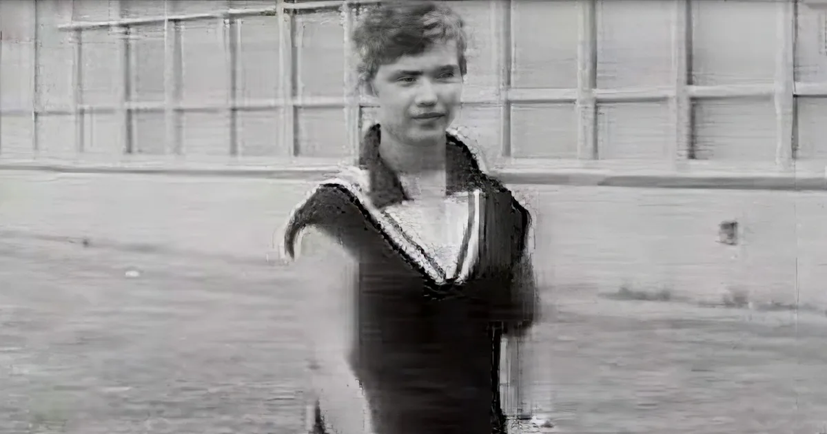 A person in a sailor-style outfit stands in front of a building with a grid-like pattern.