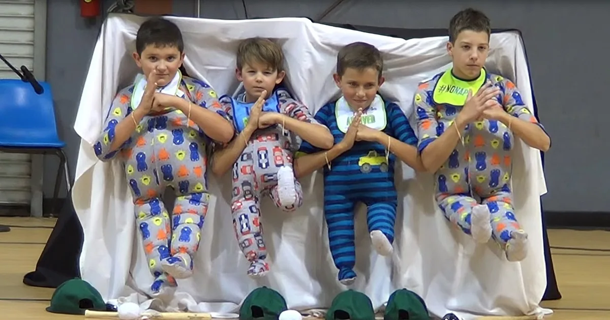 Four children in pajamas sit on a white cloth, making heart shapes with their hands.