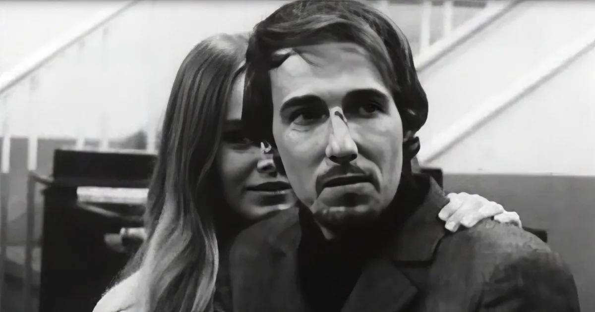 A man in a suit with a woman behind him, both looking off to the side.