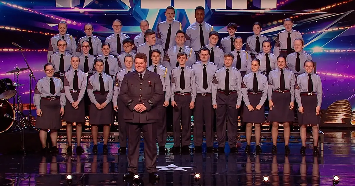 A choir in uniform stands on stage, with a conductor in front, under colorful stage lights.