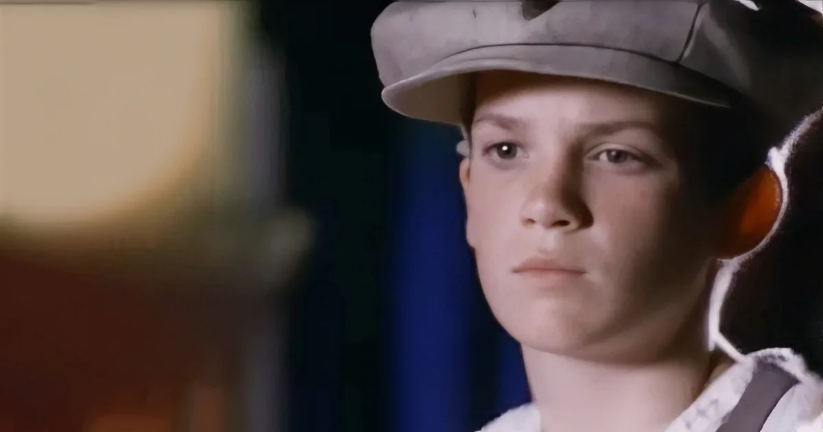 A young person wearing a hat and white shirt, looking to the side with a serious expression.