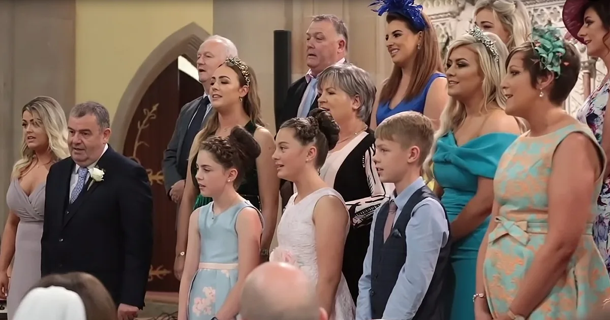 A group of people, including children and adults, dressed formally, standing together in a church setting.