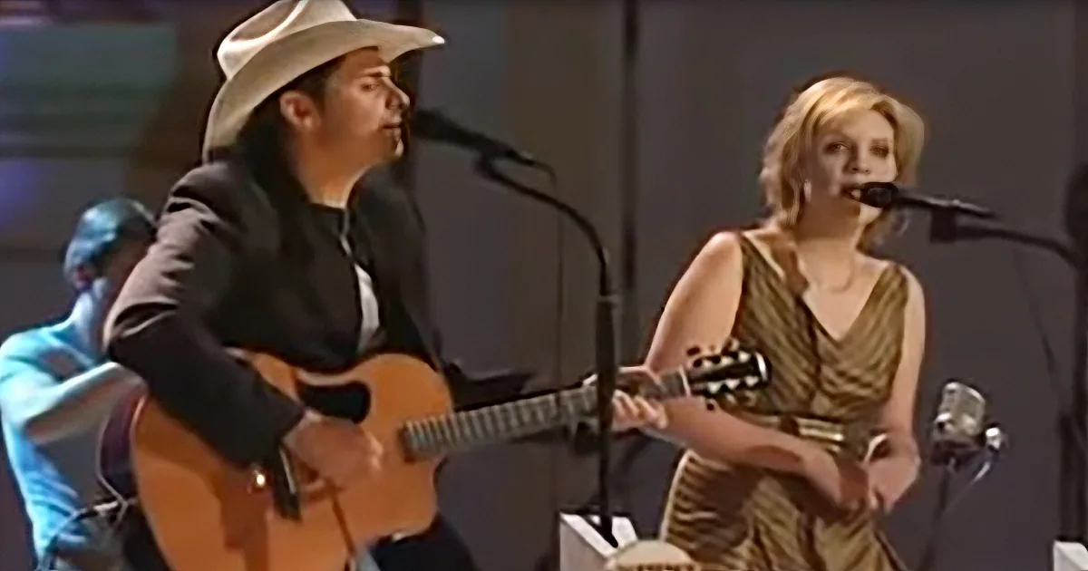A man in a cowboy hat plays guitar while a woman sings into a microphone.