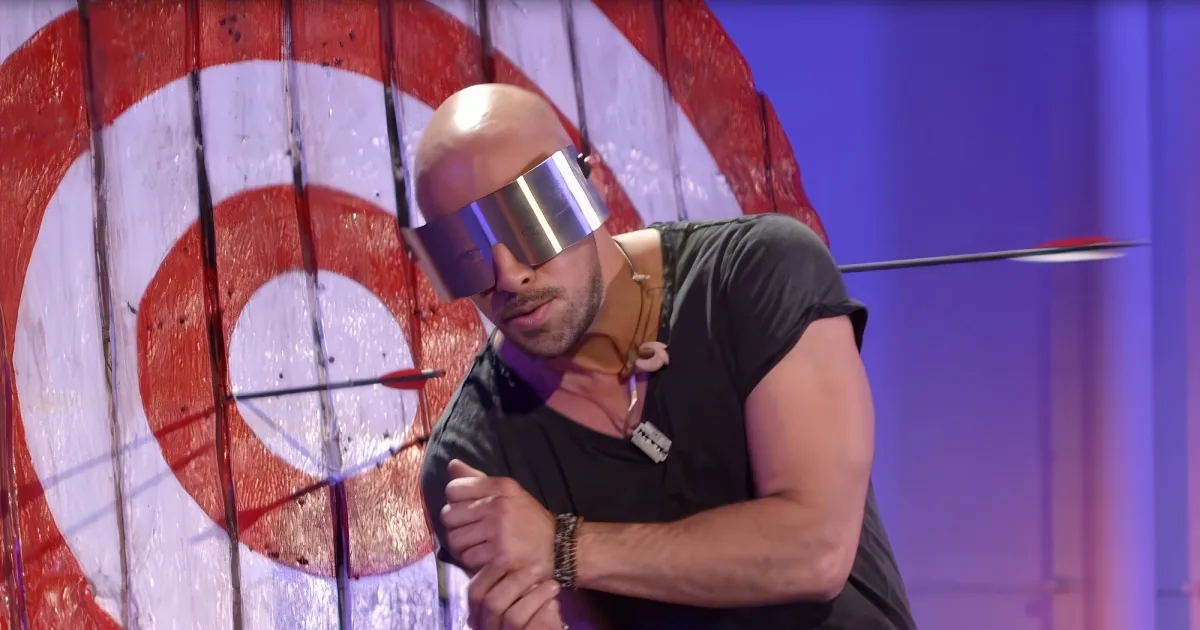 A man in a black shirt with a metallic helmet and arrows embedded in his body and arm.