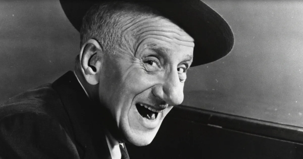 A man in a suit and hat is smiling widely, showing his teeth, in a black-and-white photo.