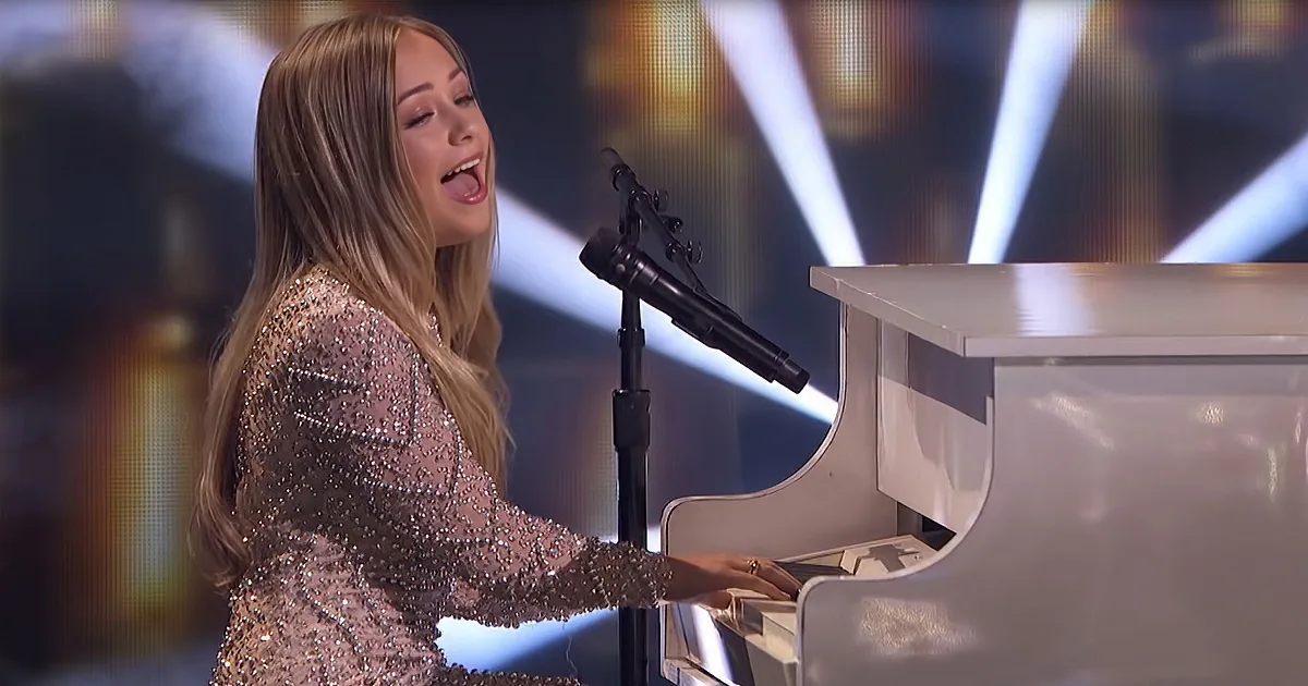 A woman in a sparkly dress sings passionately while playing a piano on stage.