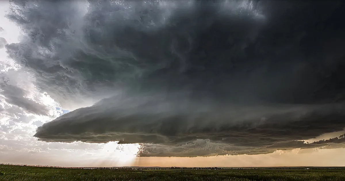 A massive, dark storm cloud dominates the sky, casting a shadow over a grassy field.