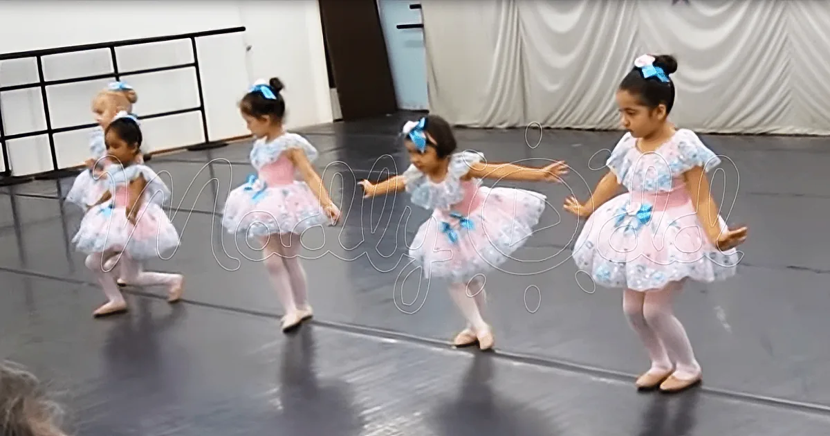 Young girls in ballet attire perform a synchronized dance routine on a stage.