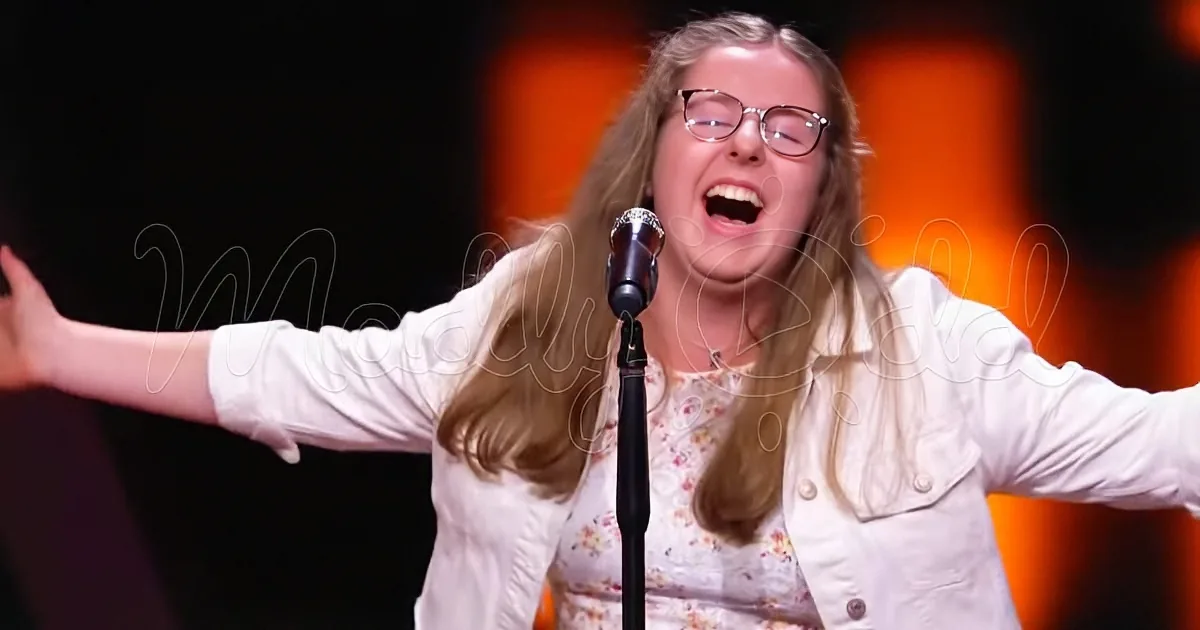 A person with long hair and glasses sings passionately into a microphone, arms outstretched.