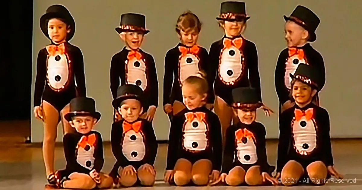 Children in penguin costumes with top hats and bow ties are posing for a group photo.