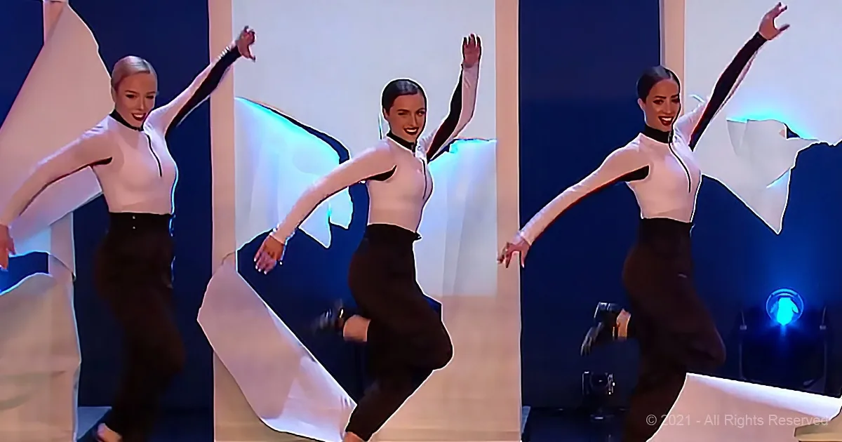 A dancer in a white top and black pants performs a dynamic pose with arms raised and a white fabric flowing behind her.