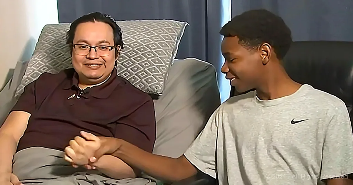 Two individuals are seated, one in a maroon shirt smiling, the other in a gray Nike shirt, both appearing engaged in a...