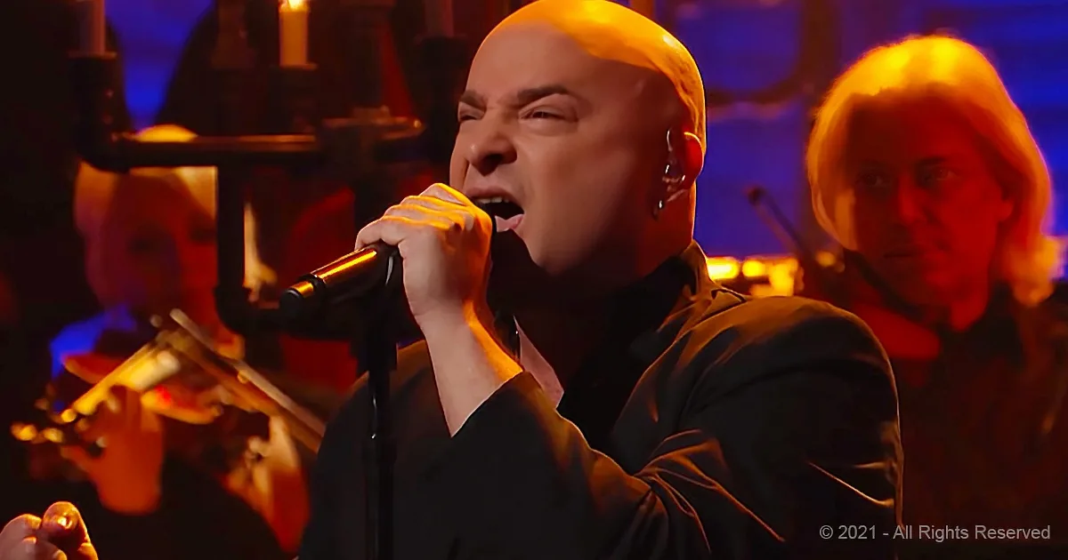 A man in a black shirt sings passionately into a microphone, surrounded by musicians.