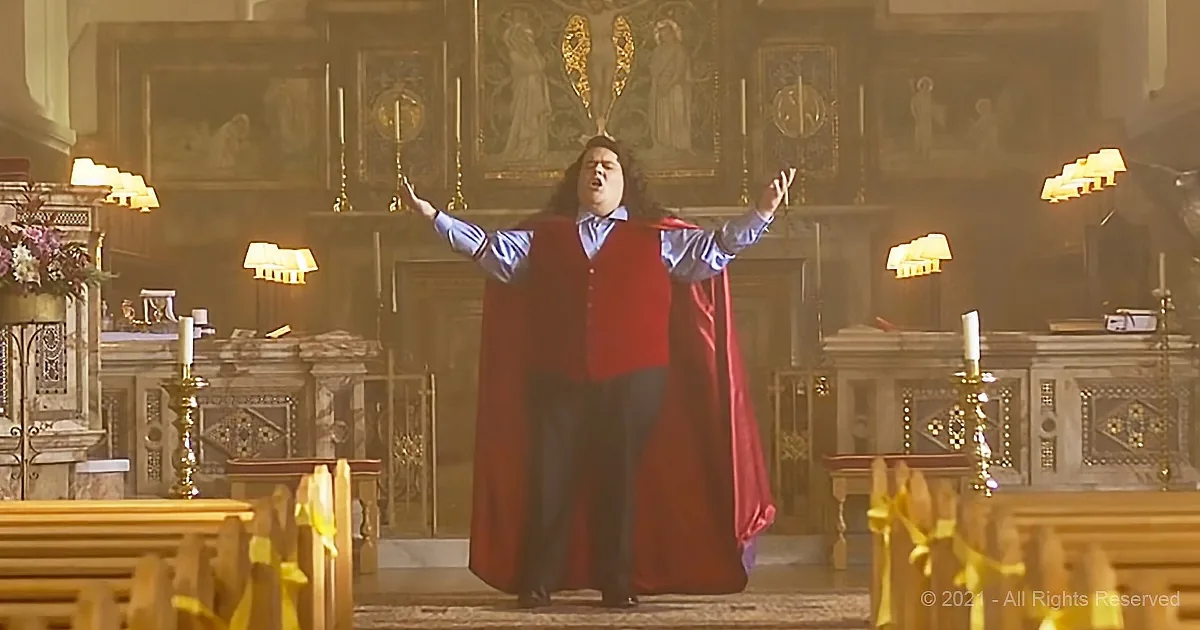 A man in a red robe stands with arms raised in a church, surrounded by ornate decorations and lit candles.