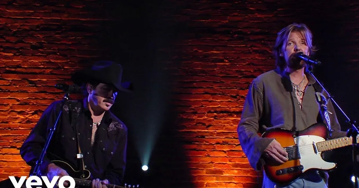 Two musicians in cowboy attire perform passionately, one playing guitar, both singing into microphones.