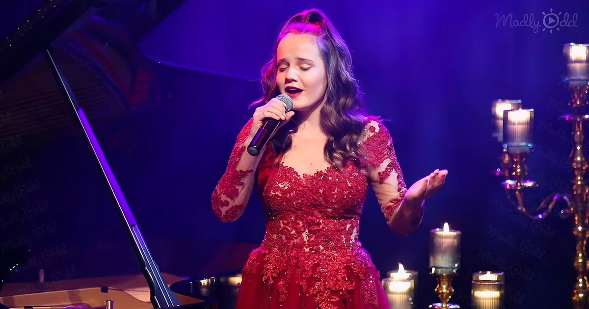 A woman in a red dress sings into a microphone on stage, surrounded by candles and a grand piano.