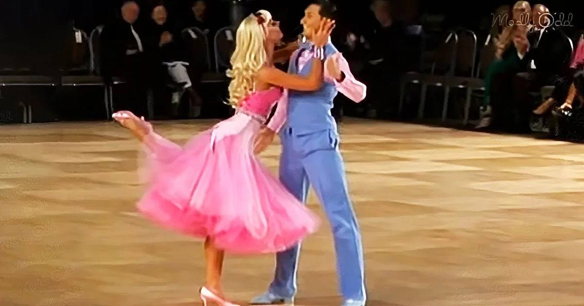 A couple in a dance competition, woman in pink dress, man in blue suit, performing a twirl.